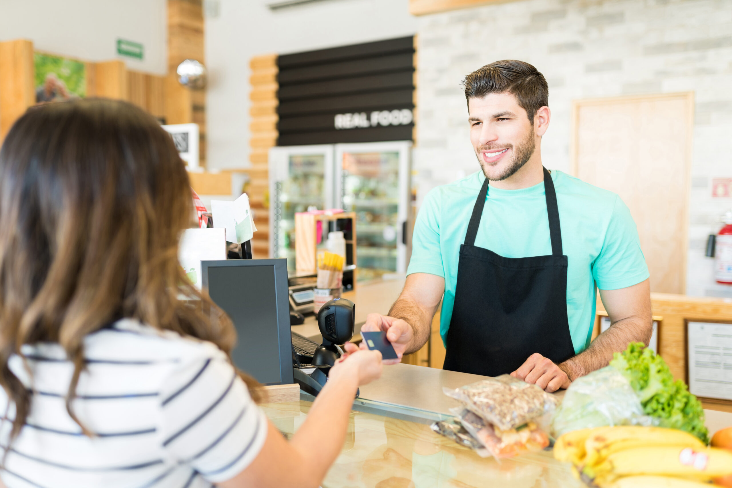 smiling male cashier receiving payment through credit card supermarket 1 scaled